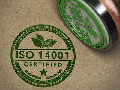 Ein grüner Stempelabdruck mit dem Text "ISO 14001 certified", daneben liegt der dazugehörige Stempel